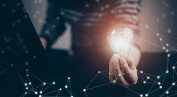 Businessman hand holding light bulb with icons and working on the desk, Creativity and innovation are keys to success.Concept of new idea and innovation with energy and power , working at home, photo