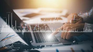businessman hand type on the laptop of company profit with colleagues partner explain with virtual dashboard statistic chart stock infographic, graphs, cryptocurrency, and new trading platforms photo