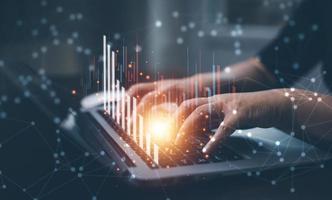 businessman hand type on the laptop of company profit with colleagues partner explain with virtual dashboard statistic chart stock infographic, graphs, cryptocurrency, and new trading platforms photo