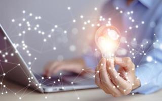 Businessman hand holding light bulb with icons and working on the desk, Creativity and innovation are keys to success.Concept of new idea and innovation with energy and power , working at home photo