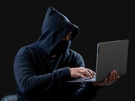 Hacker spy man one person in black hoodie sitting on a table looking computer laptop used login password attack security to circulate data digital in internet network system, night dark background. photo