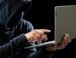 Hacker spy man one person in black hoodie sitting on a table looking computer laptop used login password attack security to circulate data digital in internet network system, night dark background. photo