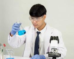 Asian male student scientist Wearing a doctor's gown in the lab looking at the chemist. caused by mixing reagents in scientific research laboratories with test tubes and microscope on the table photo