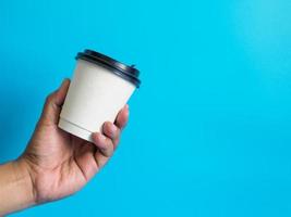 Closeup young adult man hand holding white cup paper of coffee hot drink ready to drink refreshing. aroma awake fresh to work placed on a blue isolated background. Point of view shot. photo