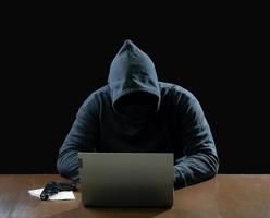 Hacker spy man one person in black hoodie sitting on a table looking computer laptop used login password attack security to circulate data digital in internet network system, night dark background. photo