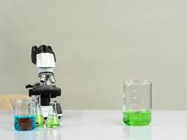 beaker and microscope for scientists was placed on a white wooden table with research reagents in the bright white room for study and work photo