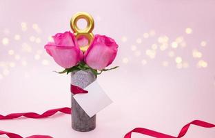 Pink roses in vase with ribbon and paper for wish on gentle background. International Women's Day, March 8, birthday. Copy space photo