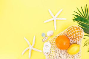 Starfish, shells with bag string bag with oranges and lemon with palm branch from the side on yellow background. Concept of summer time, vacation, travel. Copy space photo