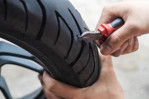 screw nail or Iron stuck puncturing motorcycle or scooter tire,mechanic repair a tire puncture from a nail or screw at motorcycle repair shop.motorcycle repair and maintenance concept photo