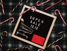 el texto de el rebaja 12.12 en el Navidad decoración letra tablero con un crédito tarjeta y un mini tienda de comestibles carro. diseño a promover el invierno rebaja a el final de el año. parte superior vista. foto