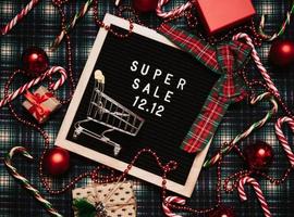 el texto de el rebaja 12.12 en un letra tablero con un rojo regalo caja y Navidad dulces, un crédito tarjeta y un mini tienda de comestibles carro. diseño a promover el invierno rebaja a el final de el año. parte superior vista. foto