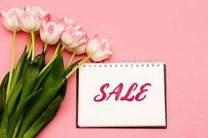 Text SALE next to a beautiful bouquet of delicate pink tulips on a pink background. There may be your text. photo