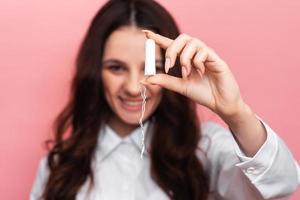 A young woman holds a menstrual swab with an applicator in her hands for easy use. Pink background. close-up. The concept of feminine hygiene. photo