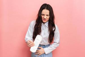 Studio shot of a young girl experiencing pain from menstruation with menstrual padding in her hands. Space for text. The concept of feminine hygiene. photo