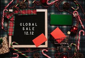 The text of the sale 12.12 on a letter board with Christmas decor, a credit card, a mini grocery cart and a phone with a chrome screen. Design to promote the winter sale at the end of the year. photo