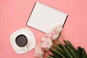 A beautiful bouquet of delicate pink tulips next to a cup of coffee on a pink background. There may be your text photo