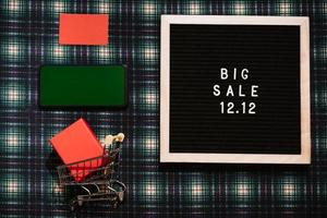 The text of the 12.12 sale is on a letter board with a gift box, a credit card, a mini grocery cart and a phone with a chrome screen. Design to promote the winter sale at the end of the year. photo