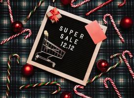 el texto de el rebaja 12.12 en un letra tablero con un rojo regalo caja y Navidad dulces, un crédito tarjeta y un mini tienda de comestibles carro. diseño a promover el invierno rebaja a el final de el año. parte superior vista. foto