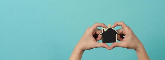 la pequeña casa de madera en las manos representa conceptos como el cuidado del hogar, el amor familiar, la vivienda, el seguro de vivienda y la hipoteca. manos sosteniendo una casa modelo pequeña aislada en el fondo del estudio verde azul. foto