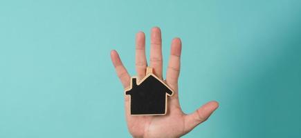 la pequeña casa de madera en las manos representa conceptos como el cuidado del hogar, el amor familiar, la vivienda, el seguro de vivienda y la hipoteca. manos sosteniendo una casa modelo pequeña aislada en el fondo del estudio verde azul. foto