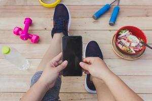 The girl holds a cell phone with exercise equipment, a wooden floor. photo