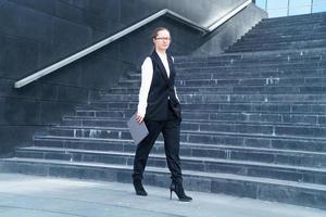 Woman realtor in jacket walks down stairs with laptop and phone in her hand photo