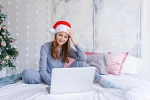 Young woman shopping online for christmas, sit on bed in blue cozy clothes photo