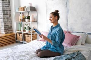 Leisure and people concept young woman reading book in bed in blue shirt photo