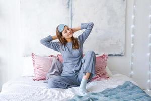 Happy healthy, beautiful young woman wearing sleep mask and blue pajamas, awake photo