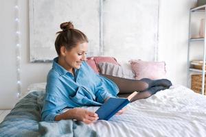 Leisure and people concept young woman reading book in bed in blue shirt photo