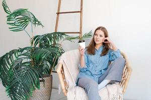 Time to relax. Smiling girl drinking hot coffee from paper cup sits in wicker photo