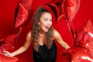 Beautiful young joyful girl is holding bunch red star balloons on red photo