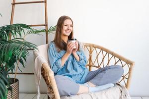 Sweet happy woman sits alone on an armchair in front curtains and looks at view photo