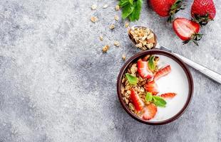 Food Background. Breakfast with yogurt, granola or muesli and strawberries on gray concrete table background. Healthy Diet Food Concept. Top view, copy space, flat lay photo