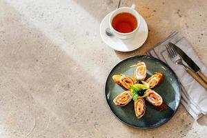 Rolls of thin pancakes with smoked salmon and cream cheese, cup of tea. Delicious and healthy breakfast or brunch. Top view with copy space. photo