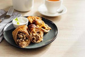 Crepes stuffed with chicken and mushrooms with sour cream and cup of tea on the wooden table. photo