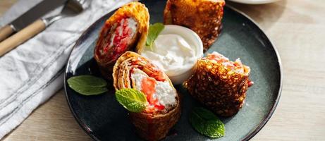 Rolls of thin pancakes with cottage cheese and sour cream on dark plate on wooden table. Delicious and healthy breakfast. Banner image for design photo