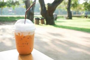 Iced milk tea with plastic takeaway glass on wood table at the garden photo