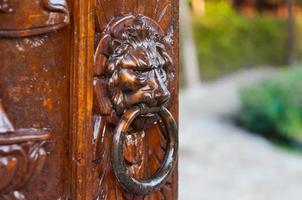 Traditional door knocker on a carve wooden door, iron made, showing the face of a lion photo