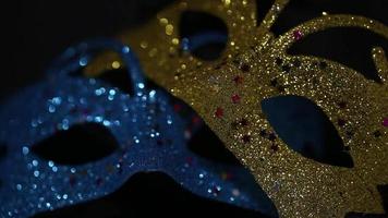 Two luxury traditional venetian masks on dark background illuminated and sparkles from the darkness. Blue and gold shiny carnival masquerade fantasy mask with small colorful stars under light in dark video