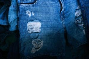 Denim jeans background. Destroyed torn classic denim blue jeans patches, banner fashion background, Stack of blue jeans on shop desk photo