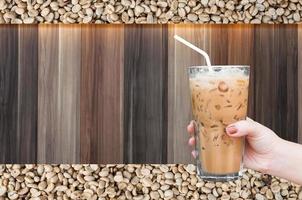 woman hand holding the glass iced coffee on wooden and raw coffee beans background,Iced latte coffee photo