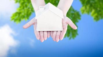 Woman hand holding small home model wooden with nature green abstract background. Family life and Business real estate concept,Eco house photo