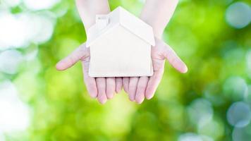 Woman hand holding small home model wooden with nature green bokeh abstract background. Family life and Business real estate concept,Eco house photo