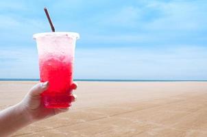 mujer encargarse de participación hielo agua italiano soda rojo en el plastico taza, rojo, dulce frio bebida en el verano a el playa, durante el Días festivos foto