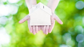 Woman hand holding small home model wooden with nature green bokeh abstract background. Family life and Business real estate concept,Eco house photo