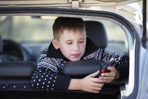A little boy is sitting in a car with a smartphone. A child on the road or on a journey. photo