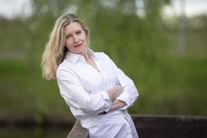 un hermosa de edad mediana europeo mujer. cincuenta años rubia mujer en un blanco camisa en el antecedentes de naturaleza. foto