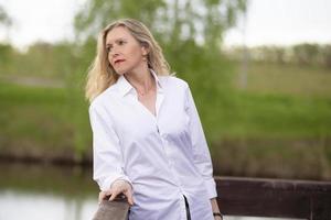 un hermosa de edad mediana europeo mujer. cincuenta años rubia mujer en un blanco camisa en el antecedentes de naturaleza. foto