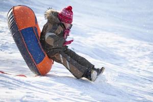 un niño feliz en el aire en un trineo de tubo en la nieve... un niño se desliza por una colina en invierno. foto